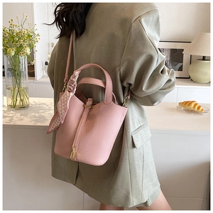 Pink lychee grain leather bucket bag with silk scarf on handle and shoulder strap detail