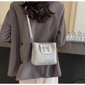 Detailed view of a silver bucket bag with textured finish and metal bow buckle decoration