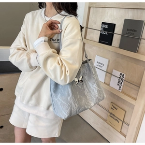 Detail of silver-blue metallic tote bag with butterfly ornament on casual cream outfit