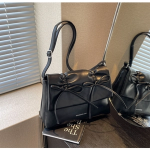 Détail de sac à main plissé noir avec nœuds et bandoulière réglable sur surface miroir