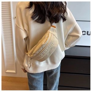 Detail of off-white canvas chest bag featuring letter embroidery and orange brand tag
