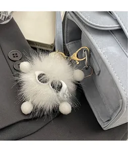 Detail of white plush pom-pom keychain with cartoon glasses on light blue handbag