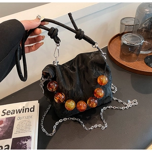 Close-up of black pleated handbag featuring amber bead accents and a silver chain strap