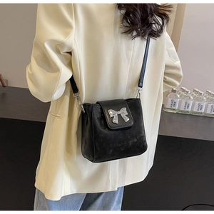 Close-up of black crossbody bucket bag with silver bow accent on beige blazer jacket