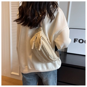 Detail of beige crossbody bag featuring letter embroidery and rope zipper pullers