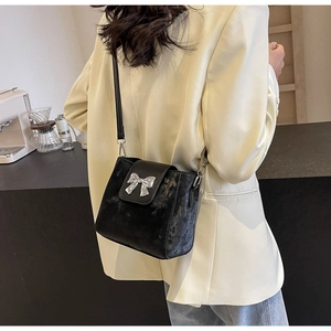 Detail of black bucket bag with silver bow buckle on model in beige blazer