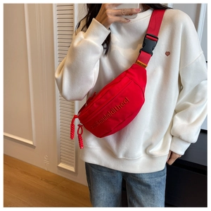Detail of red fabric waist bag showing embroidered letters and adjustable strap with buckle