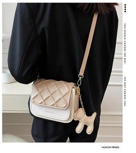 Gros plan du sac bandoulière matelassé beige avec chaîne dorée et breloque chien