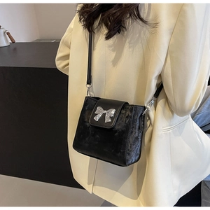 Detail of black velvet crossbody bucket bag featuring a silver metal 3D bow decoration