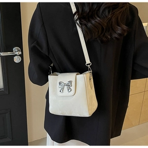 Detail of cream crossbody bucket bag with silver bow buckle and leather strap on model
