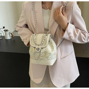Close-up of mini cream-white backpack with gold butterfly print and silver chain strap