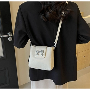 Detail of a chic cream leather bucket bag with silver bow accent worn by a model