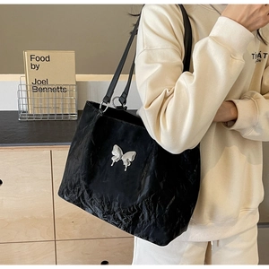 Detail of black pleated tote bag with silver butterfly emblem and leather shoulder straps