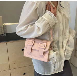Pink matte square crossbody bag with decorative buckles and a white plush charm