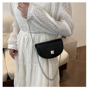 Detail of a mini black saddle bag with silver chain strap worn over a white dress