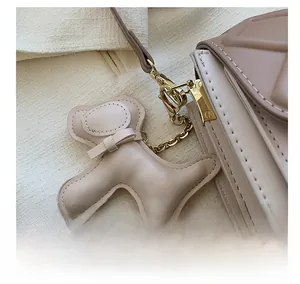 Gros plan du pendentif chiot crème avec chaîne dorée sur un sac à bandoulière matelassé