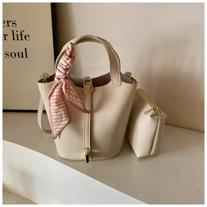 Detail of cream bucket bag with lychee texture, gold lock, and silk scarf handle