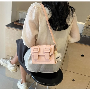 On-body view of a pink crossbody bag with a matte finish and cute white pompom charm