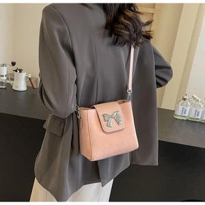 Pink bucket bag with silver bow accent worn by a model in a cozy cafe setting