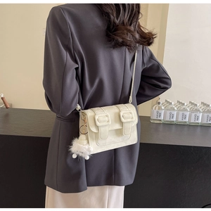 White leather crossbody bag with decorative buckles and fuzzy pom-pom charm on grey suit