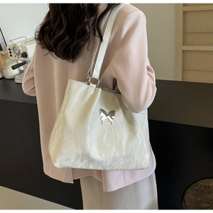Detailed close-up of butterfly metal ornament on cream white pleated tote bag