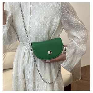 Detail of a mini green leather saddle bag with silver chain and metal stud on a white dress