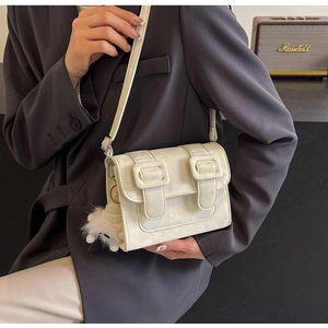 Detail of cream crossbody bag with square buckles and plush dog charm on a gray blazer