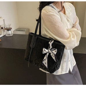 Detail of black tote bag with textured surface and fashion scarf on handle in cafe setting