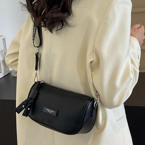 Chic black cylinder crossbody bag with wide logo strap worn by a model in a beige suit