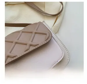 Détails de la texture matelassée et du logo doré sur le mini sac bandoulière beige