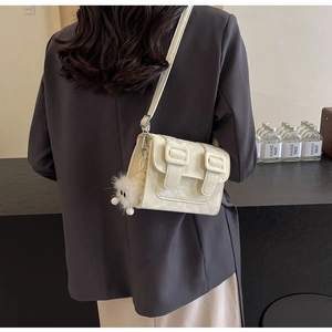 Cream crossbody bag with decorative buckles and plush ball charm worn by a model