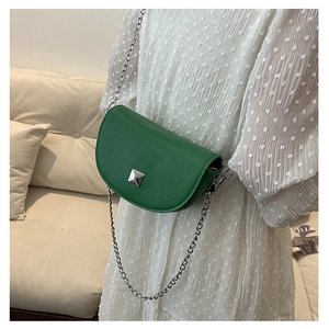 Close-up of green leather saddle bag with silver chain strap on white dress