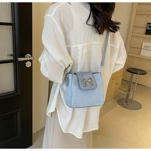 Detail of light blue suede bucket bag featuring a silver metal bow and slender strap