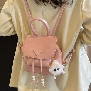 Pink mini backpack with plush monster charm and triangular logo on a cream blazer model