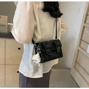 Model wearing a black vintage matte leather crossbody bag with dual buckles and pompom