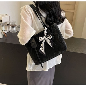 Detail of a black textured tote bag with a fashion bow scarf in a cafe setting