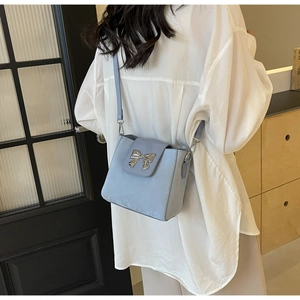Detail view of light blue bucket bag with silver bow accent on a female model