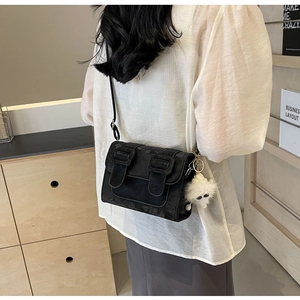 Chic black crossbody bag with large buckles and plush charm on a casual outfit