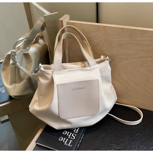 Détail du sac cabas en nylon crème avec poche en cuir kaki sur fond de bois naturel