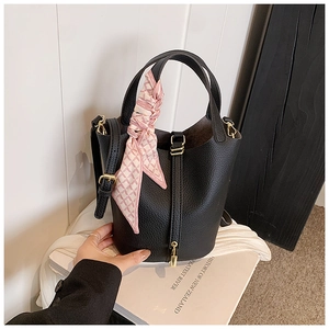 Detail of black lychee leather bucket bag with pink silk scarf on handle and gold lock