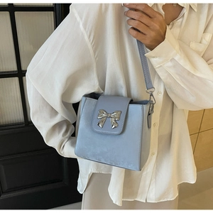 Detail of light blue bucket bag featuring a silver metal bow clasp and sleek shoulder strap