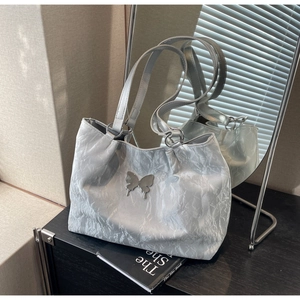 Detailed view of silver butterfly metal charm and wrinkled metallic tote bag texture