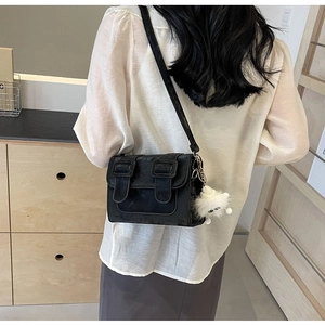 Detail of black satchel bag with white pompom worn by model in minimalist indoor setting