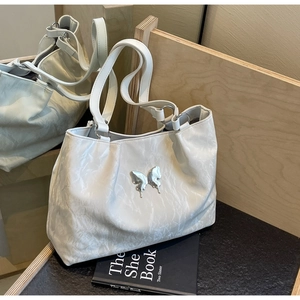 Detail of cream pleated tote bag with silver butterfly charm on a textured background