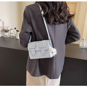 Detail of light blue crossbody bag with dual buckles and fluffy monster charm on model