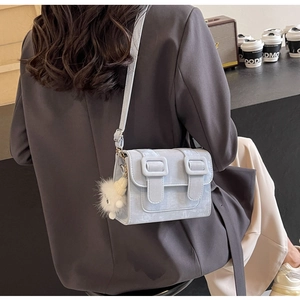Close-up of light blue flap crossbody bag with double buckle and plush charm detail