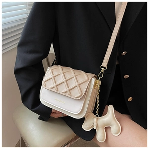 Détail d'un sac à bandoulière matelassé beige avec quincaillerie dorée et breloque chien