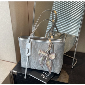 Detail of silver pleated tote bag with fashion scarf bow decoration on smooth surface