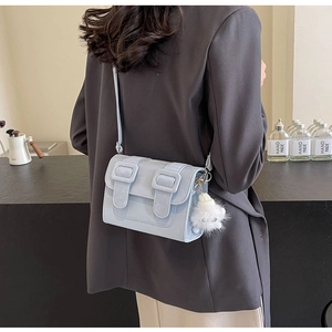 Side view of light blue crossbody bag with white fur ball charm on gray blazer