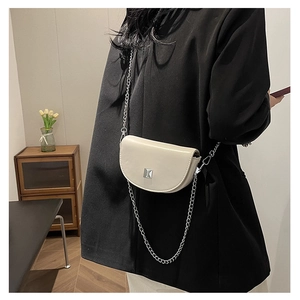 Chic cream mini saddle bag with silver chain strap worn over a stylish black blazer